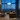 A modern living room with a large white arched floor lamp beside a brown sectional sofa, with a city skyline visible through tall windows at dusk.